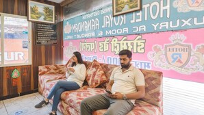 A hotel reception area with a reception desk, a sofa with two people sitting, and a wall with a signboard. - Fabhotel Royal Aanandam (Gwalior)