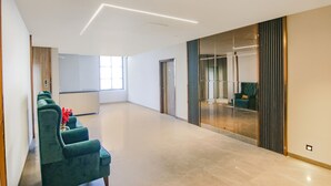 A spacious, modern hotel lobby with a long reception desk, a seating area with green upholstered chairs, and a large glass partition. - Fabhotel Prime K9 Grand (Ludhiana)
