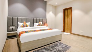 A modern hotel room with a large bed, a grey upholstered headboard, and a wooden door. - Fabhotel Prime K9 Grand (Ludhiana)