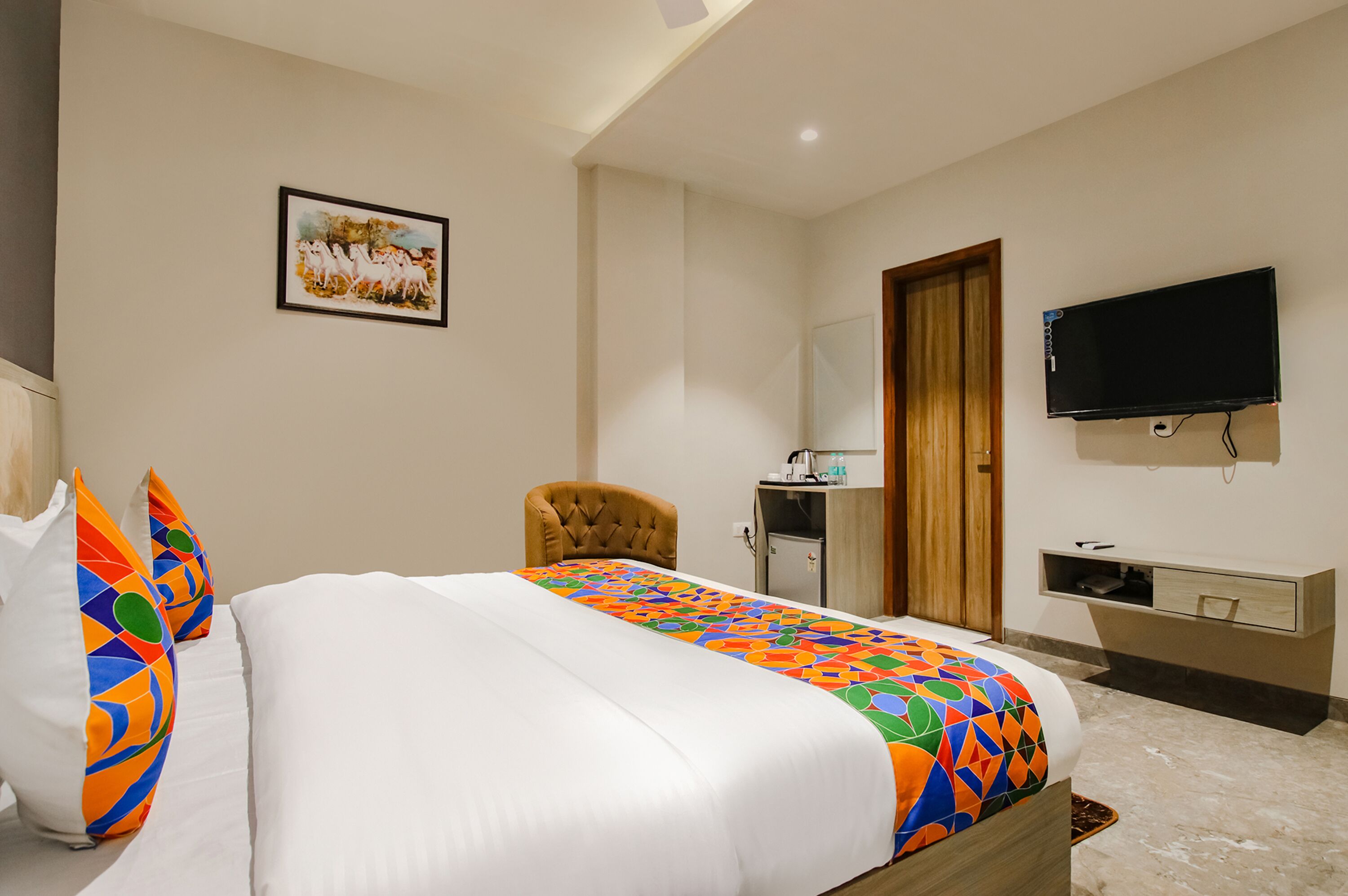 Una habitación de hotel con cama, una silla, un escritorio, televisor y armario.