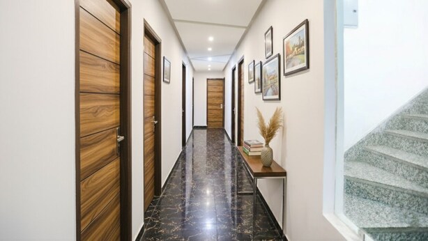 Um corredor com portas de madeira, chão de mármore, quadros nas paredes e uma pequena mesa com um vaso.