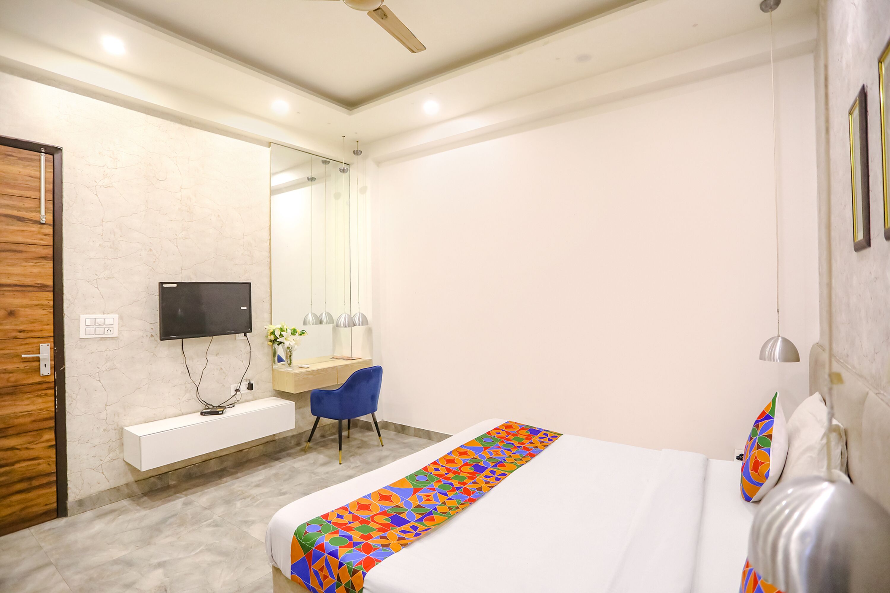 A modern hotel room with a large bed, a desk with a chair, a flat-screen TV, and a bathroom with a mirror and sink.