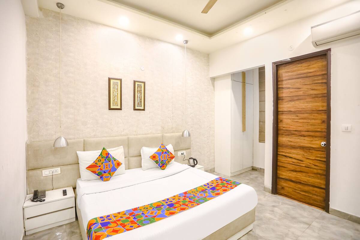 Un dormitorio moderno con una cama grande, dos mesitas de noche, una mesita auxiliar, una puerta de madera y un equipo de aire acondicionado instalado en la pared.