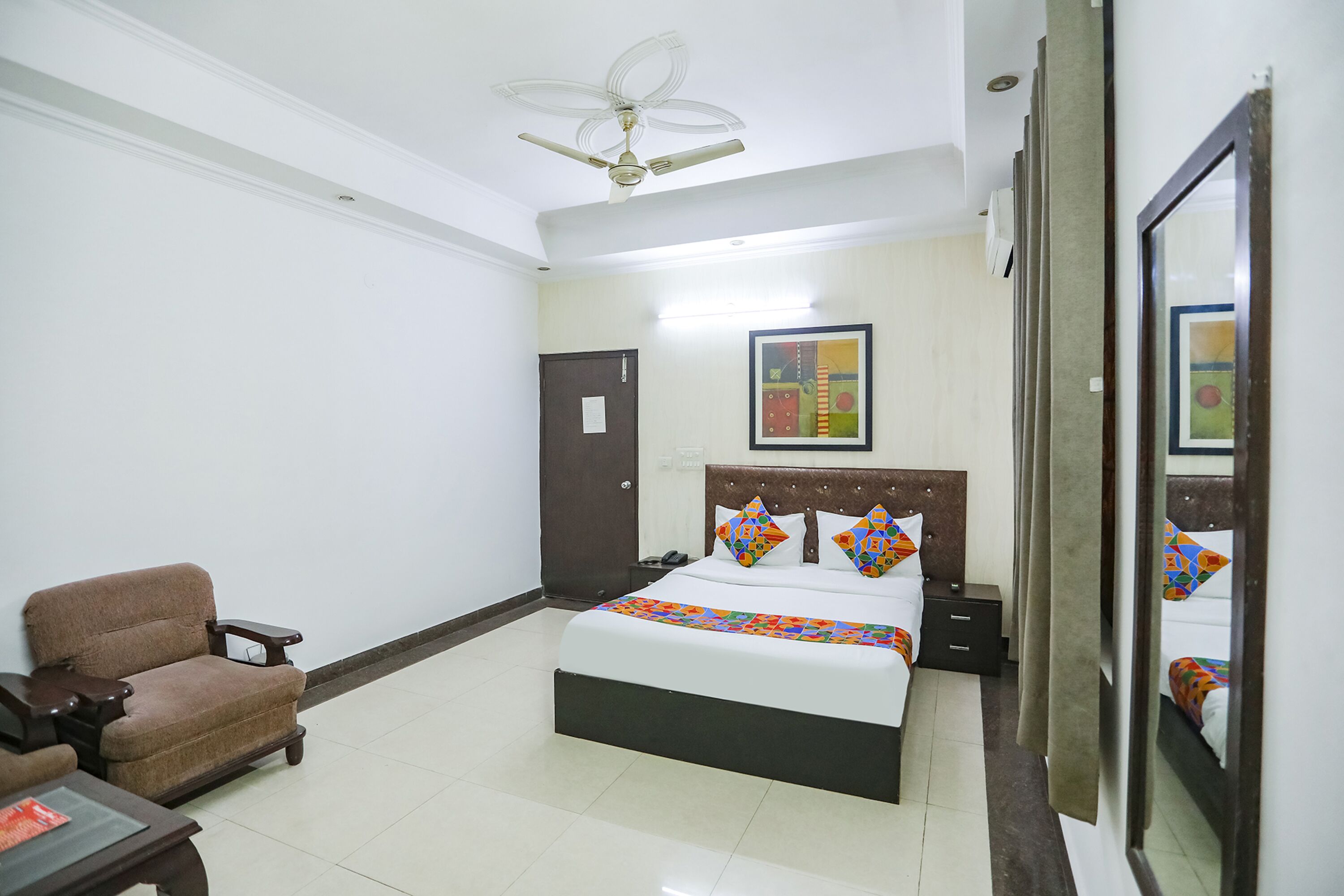 A hotel room with a bed, a chair, a desk, and a ceiling fan.
