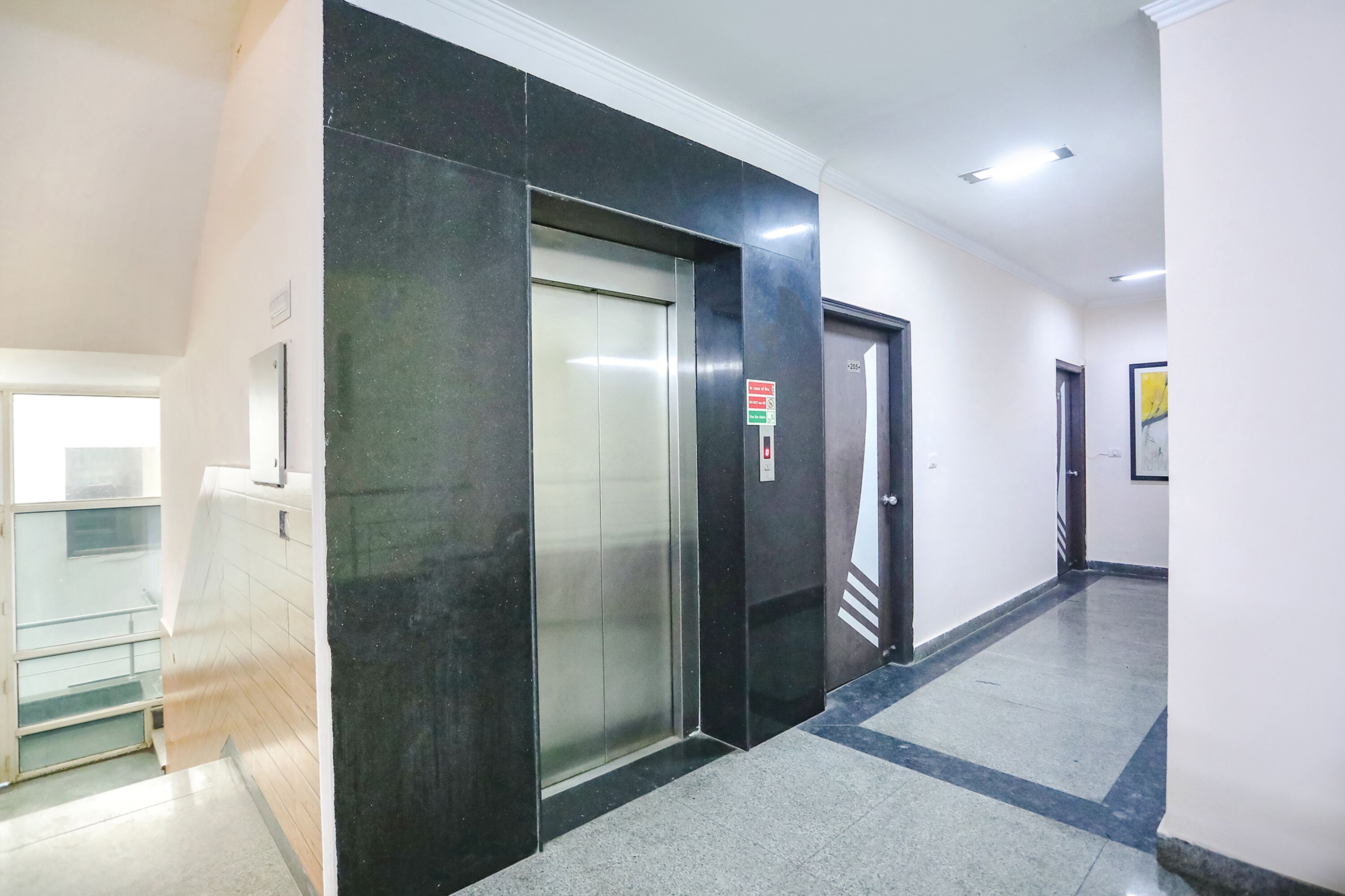 A hallway with a glass elevator door, a door with a red sign, and a tiled floor.