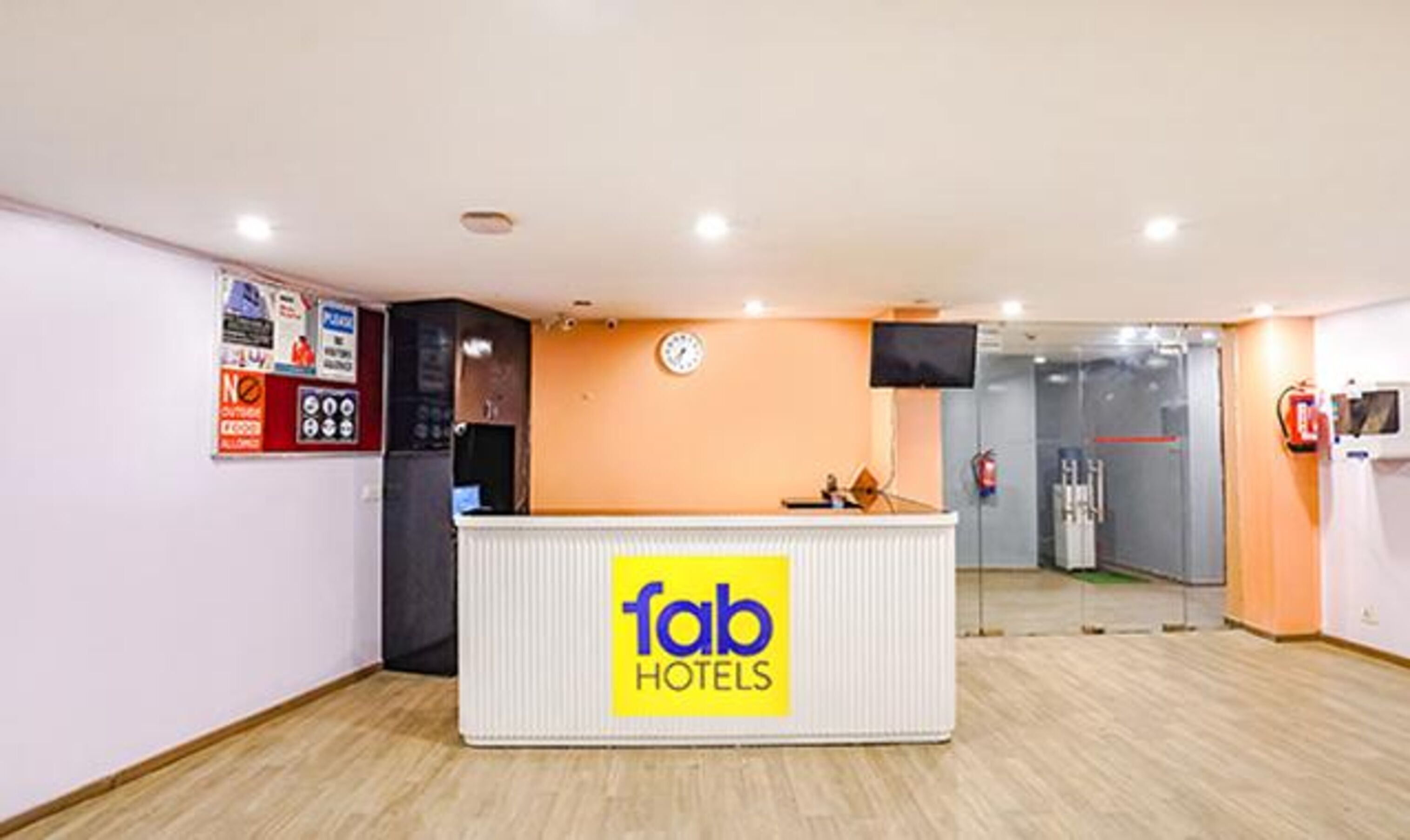 A reception desk with a 'fab hotels' sign, a clock, and a fire extinguisher on the wall.