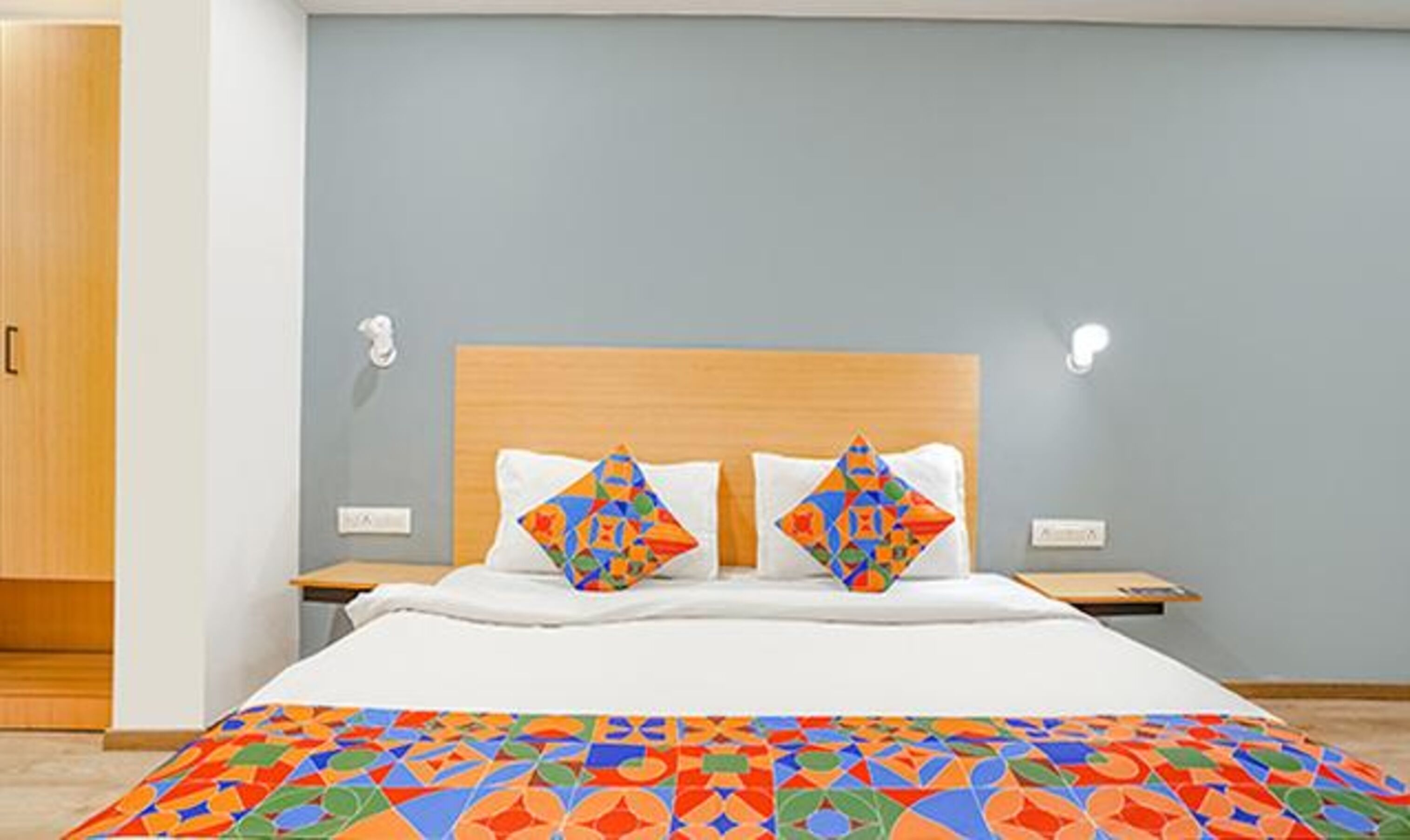 Un dormitorio con cama, dos mesitas de noche, cabecera de madera y edredón de estampado geométrico y colores vivos.