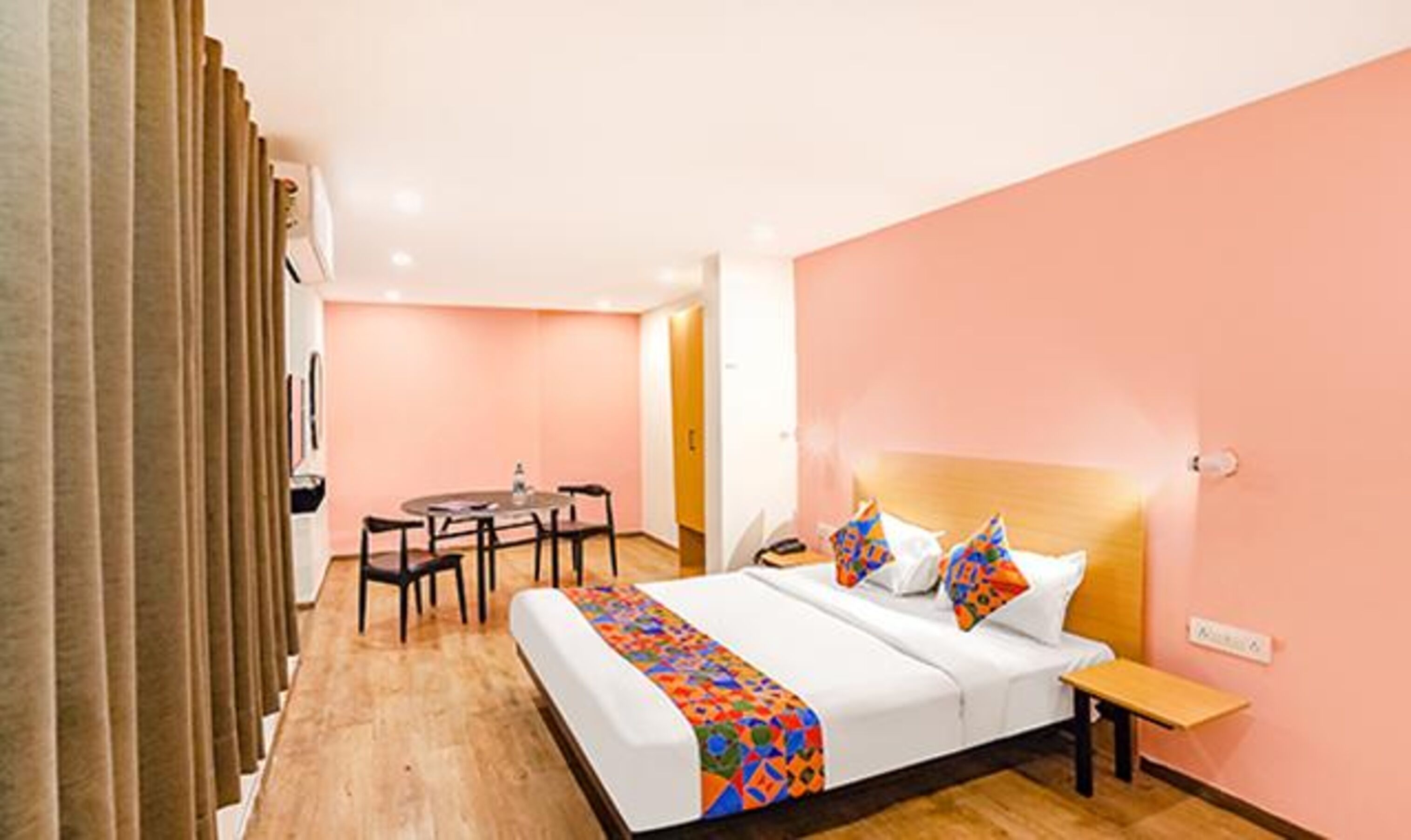 A hotel room with a bed, bedside table, and a small desk with chairs.