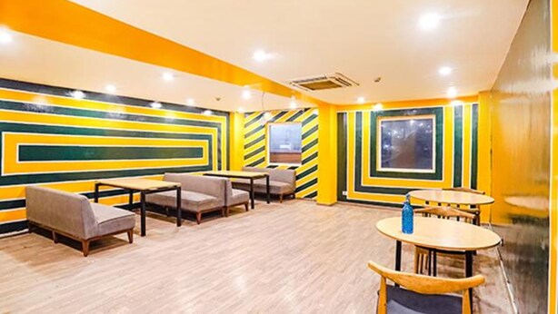 A room with a modern design, featuring a wooden floor, a sofa, a table, and a chair. - FabHotel Noida Grand (Noida)