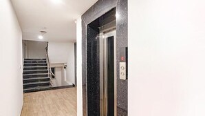 A modern elevator with a marble finish, a staircase with a handrail, and a light-colored wooden floor. - FabHotel Noida Grand (Noida)