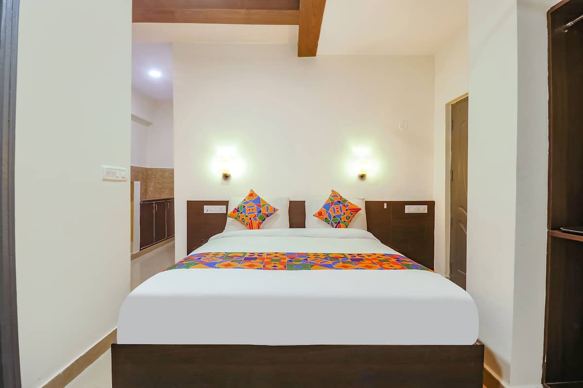 A neatly made bed with a white bedspread and colorful geometric pillows, two wall-mounted lights, and a wooden headboard.