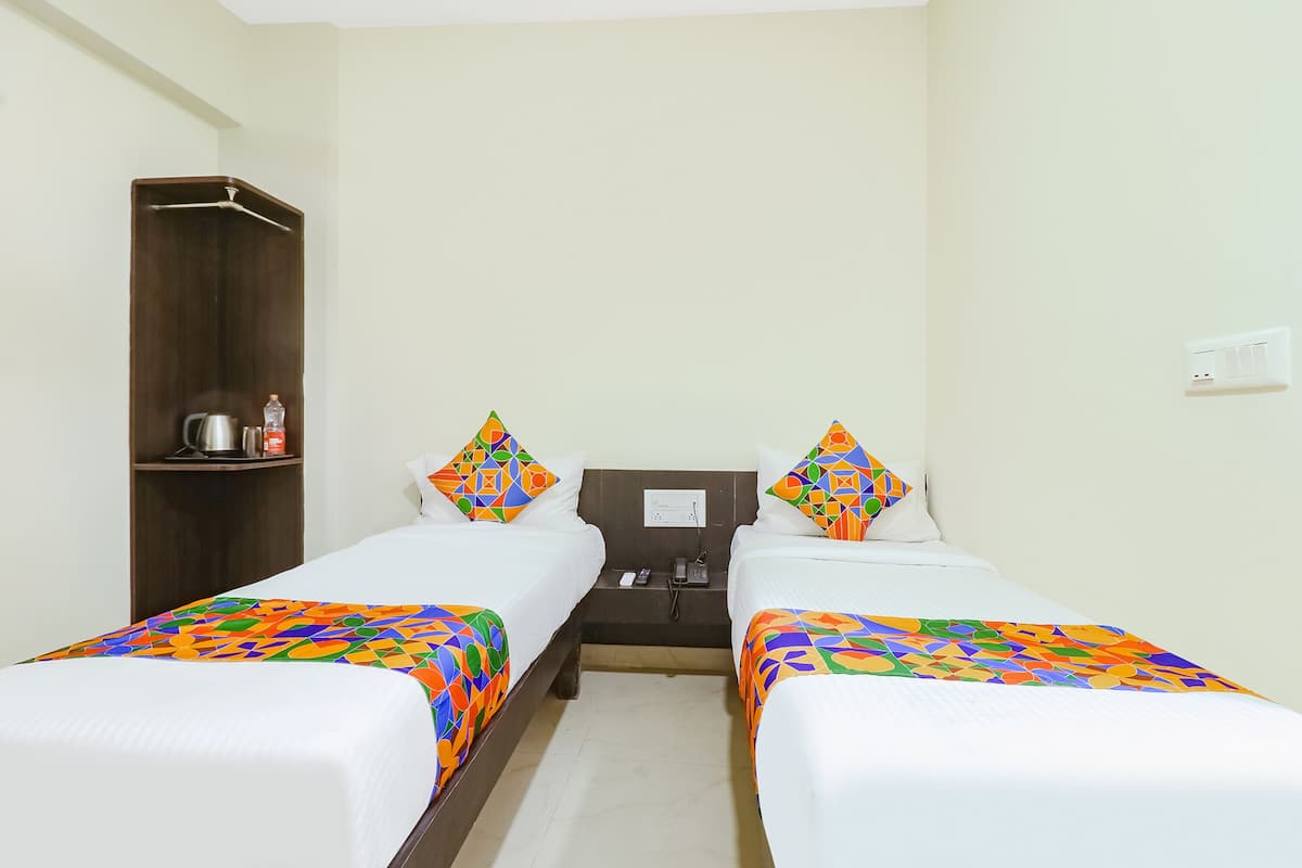 A hotel room with two beds, each with colorful bedding and matching pillows. There is a wooden wardrobe and a small table with a kettle and a bottle.