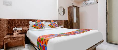A neatly arranged hotel room with a bed, a nightstand, a wardrobe, and an air conditioning unit.