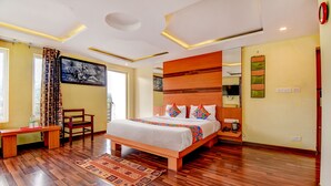A hotel room with a wooden bed, a desk, a chair, and a large window. - Fabhotel Abirami Grand Inn (Kodaikanal)
