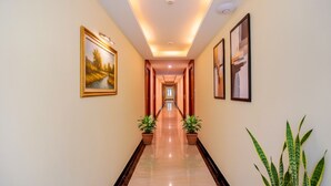 A long, well-lit hallway with a polished floor, flanked by potted plants and framed artwork on the walls. - Fabhotel Abirami Grand Inn (Kodaikanal)