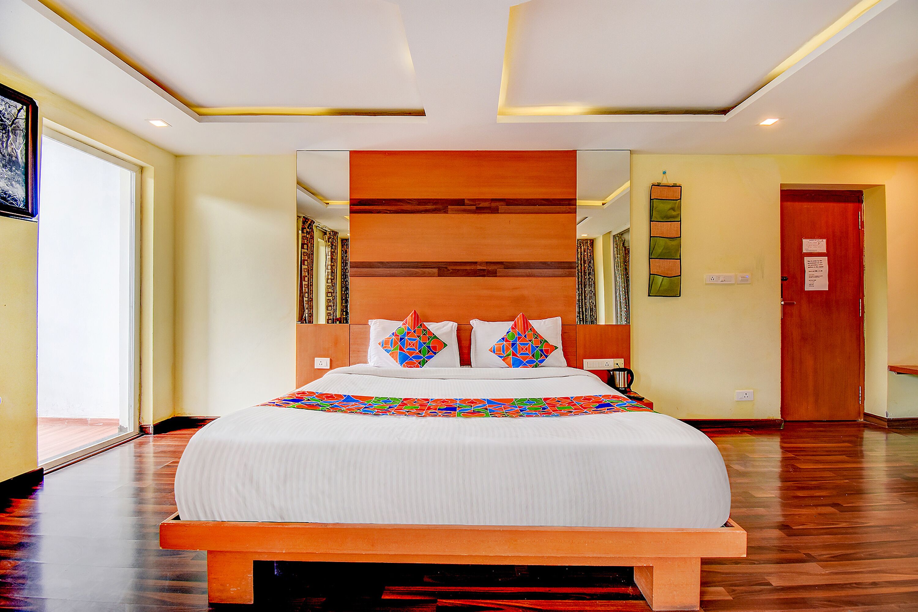 Una cama bien tendida con una colcha de diseño geométrico y colores vivos, un cabecero de madera y un espejo encima.