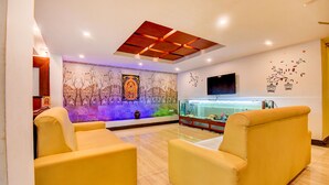 A modern lobby with a fish tank, comfortable seating, a mural, and a flat-screen TV. - Fabhotel Abirami Grand Inn (Kodaikanal)