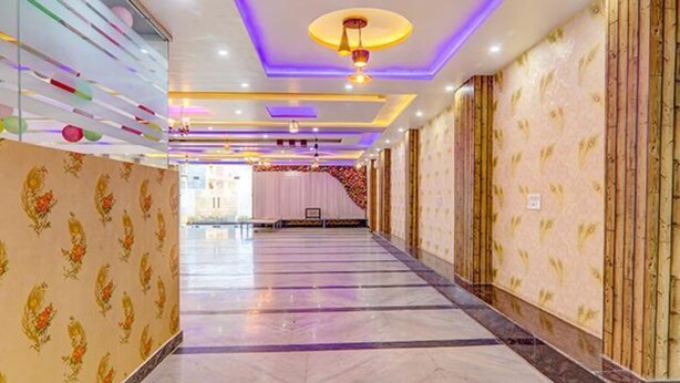 A hotel corridor with patterned wallpaper, a marble floor, and a stage area in the distance. - Fabexpress Ss Grand (Lucknow)