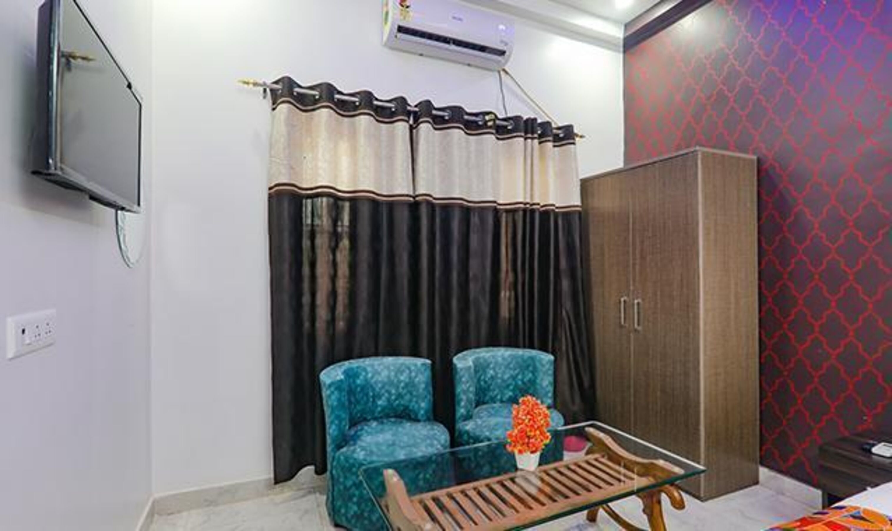 Una habitación con dos sillones azules, una mesa de centro de madera con un florero y un armario. También hay un televisor montado en la pared.