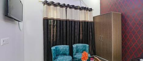 Una habitación con dos sillones azules, una mesa de centro de madera con un florero y un armario. También hay un televisor montado en la pared.