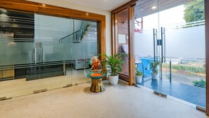 En moderne hotellobby med glasfacade, trappe og krukker med planter.