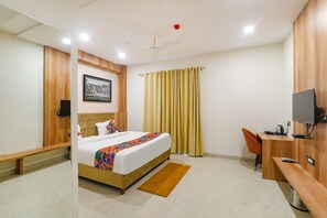A hotel room with a bed, a desk, a chair, a television, and a ceiling fan.