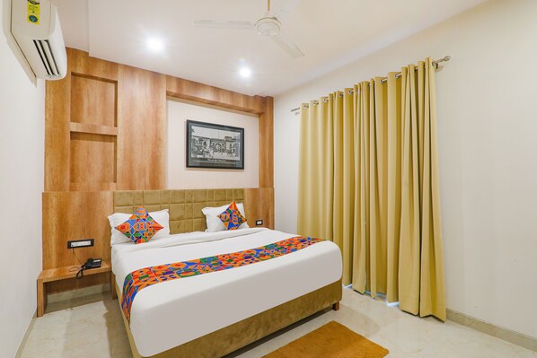 A hotel room with a bed, a ceiling fan, a wall-mounted air conditioner, a framed picture, and a window with curtains.