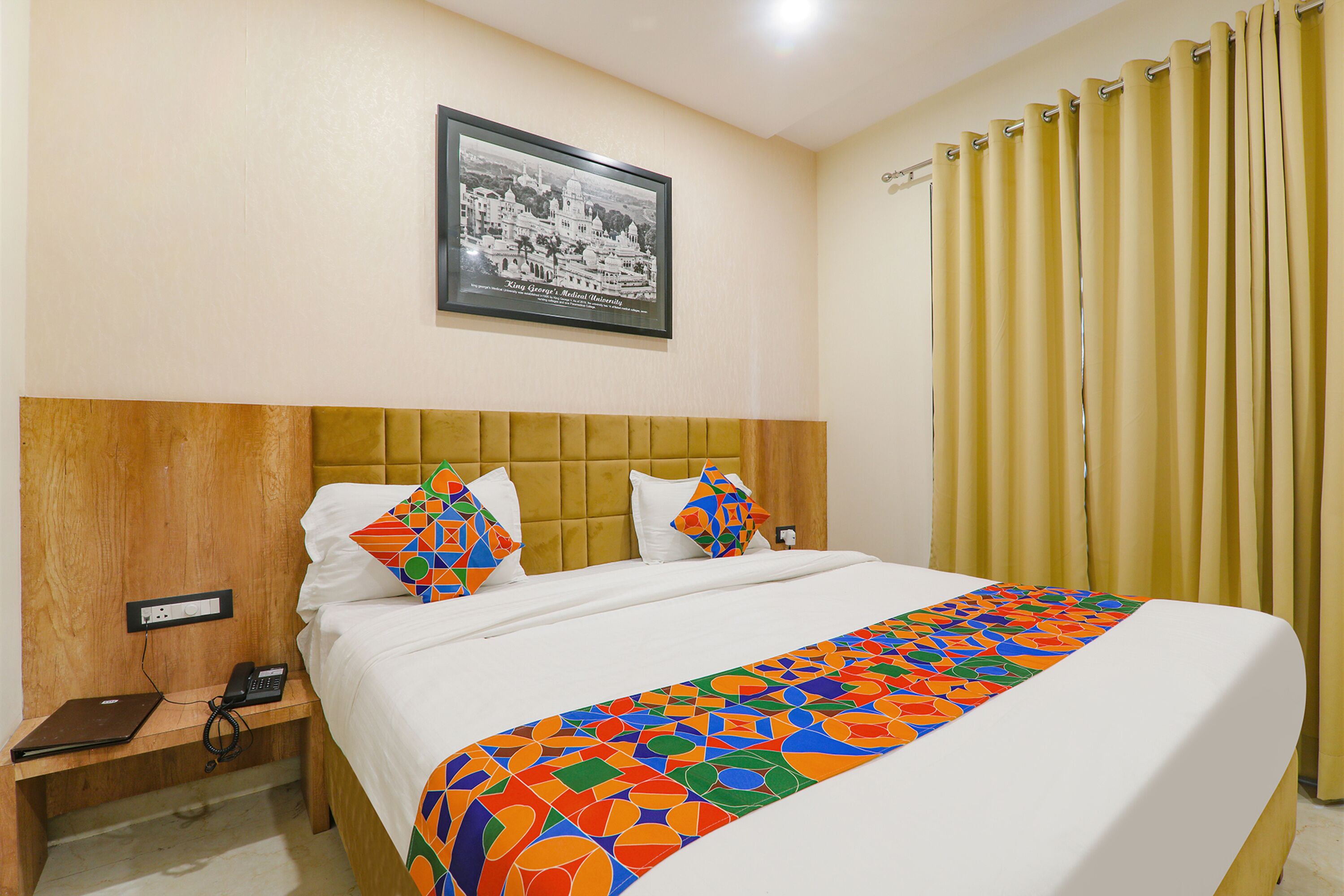 Habitación de hotel con una cama, una mesita de noche, un teléfono y un cuadro enmarcado en la pared.