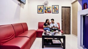 A modern living room with a red sofa, a glass coffee table, and abstract art on the wall. - FabHotel Pratiksha (Ahmedabad)