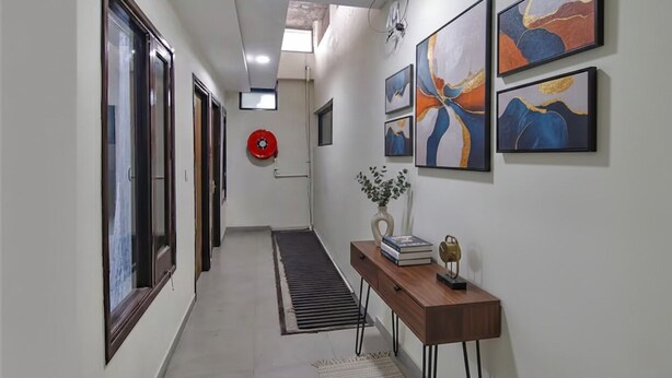A hallway with a wooden console table, abstract paintings, and a red fire extinguisher. - FabHotel Golden Gate I Amritsar (Amritsar)