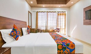 Une chambre d’hôtel avec un grand lit, une tête de lit en bois, une fenêtre avec des rideaux, une chaise et un téléviseur à écran plat fixé au mur.
