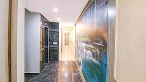 A hallway with a marble floor, a painting of a waterfall, and a door at the end. - FabHotel Welcome Residency (Dera Bassi)