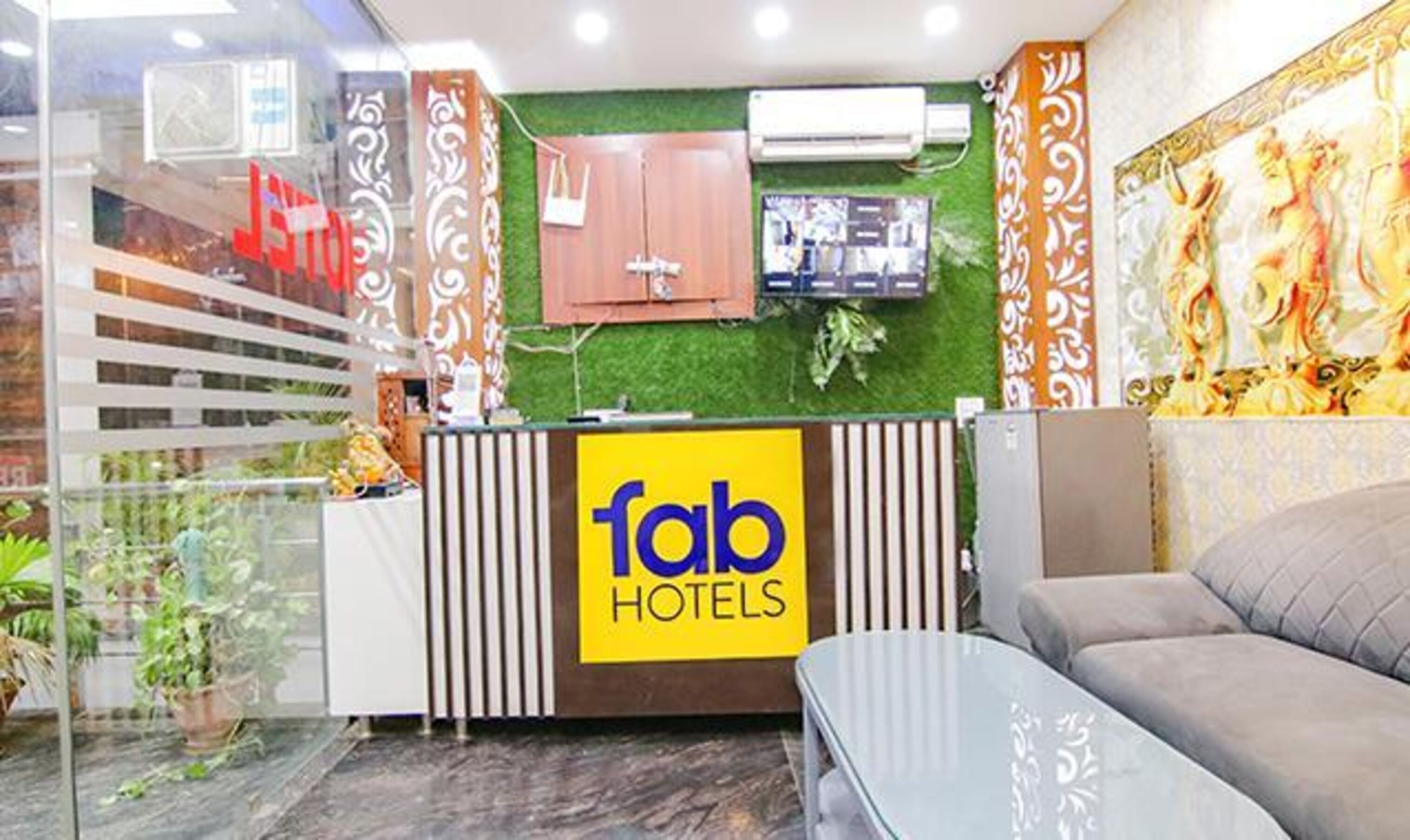 A hotel reception area with a green wall, a 'Tab Hotels' sign, a wooden cabinet, and a sofa.