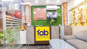 A hotel reception area with a green wall, a 'Tab Hotels' sign, a wooden cabinet, and a sofa. - FabHotel Welcome Residency (Dera Bassi)