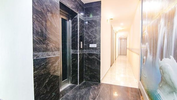 A hallway with marble walls and a glass elevator. - FabHotel Welcome Residency (Dera Bassi)
