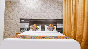 A hotel room with a white bed, a colorful bedspread, a brick-patterned wall, and a wooden headboard. - FabHotel Welcome Residency (Dera Bassi)