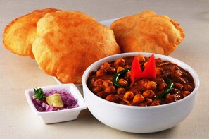 A bowl of chickpea curry with a side of sliced onions and lemon, accompanied by two pieces of bread. - Via Airport Stay Inn - Nr, Rajiv Gandhi International Airport (Hyderabad)