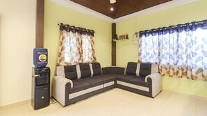 A living room with a sectional sofa, a television, and a ceiling fan. - Via Airport Stay Inn - Nr, Rajiv Gandhi International Airport (Hyderabad)