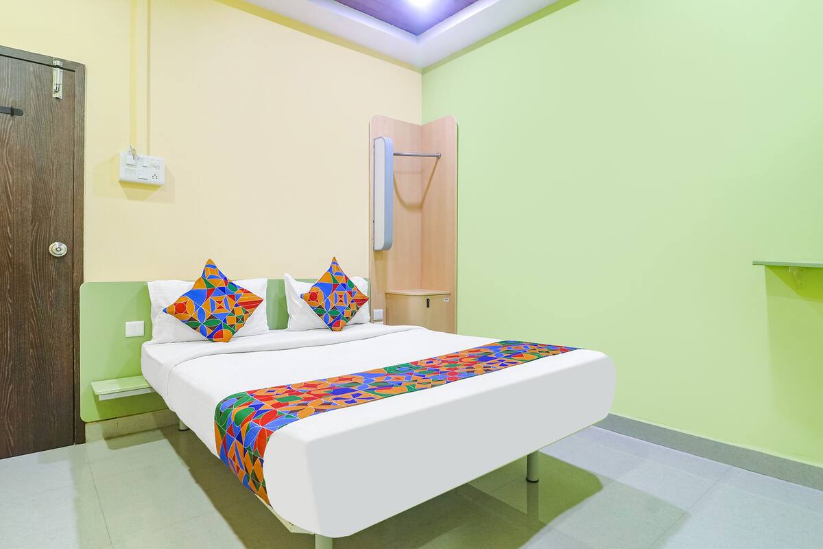 A hotel room with a bed, two pillows, a bedside table, a nightstand, and a wall-mounted towel rack.