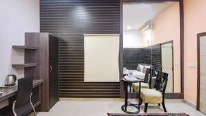 A compact room with a bed, a desk, and a chair. There is a mirror on the wall and a window with blinds. - FabExpress Gardenia (Kolkata)