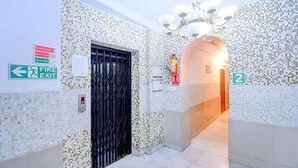 A hallway with a fire exit sign, a door, and a number indicating the room. - FabExpress Gardenia (Kolkata)