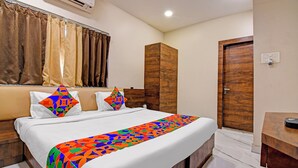 A hotel room with a bed, a wooden wardrobe, a bathroom with a wooden door, and a window with curtains. - Fabhotel Dak Plaza (Barasat)