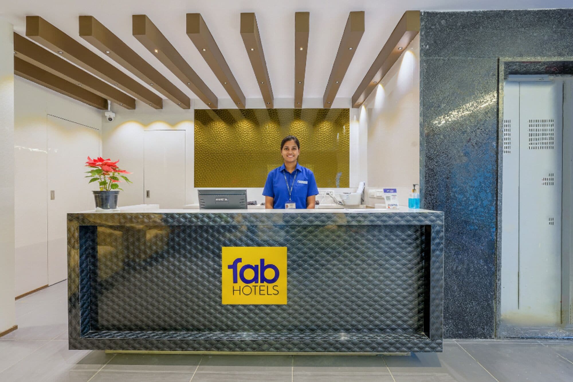 A reception desk with a '1ab Hotels' sign, a receptionist, and a potted plant.