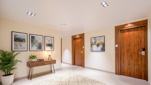 A hallway with a wooden door, a potted plant, a console table with books, and framed artwork on the walls. - Fabhotel Phoenix Brookfield (Bengaluru)