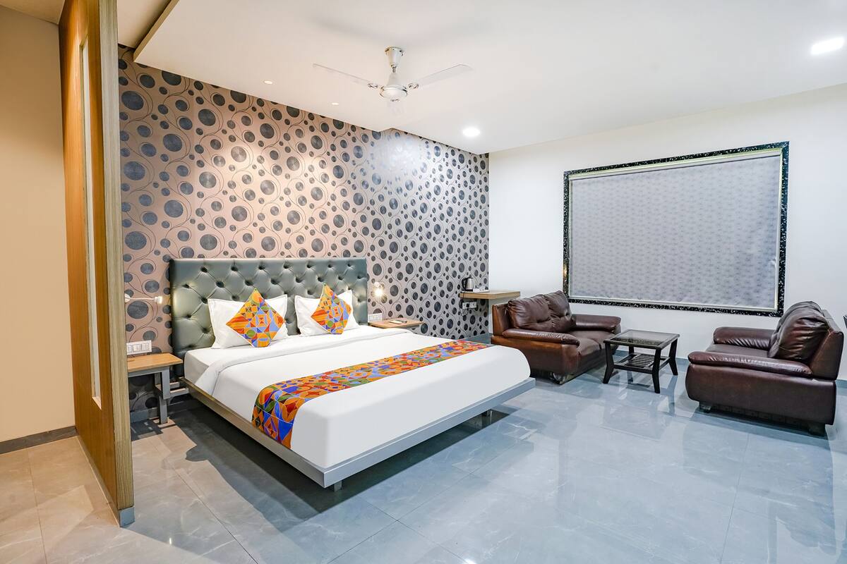 A modern hotel room with a large bed, a leather sofa, a small table, and a large window.