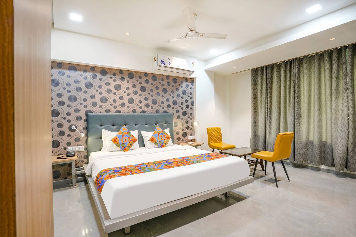 A modern hotel room with a large bed, a desk, a chair, and a ceiling fan.