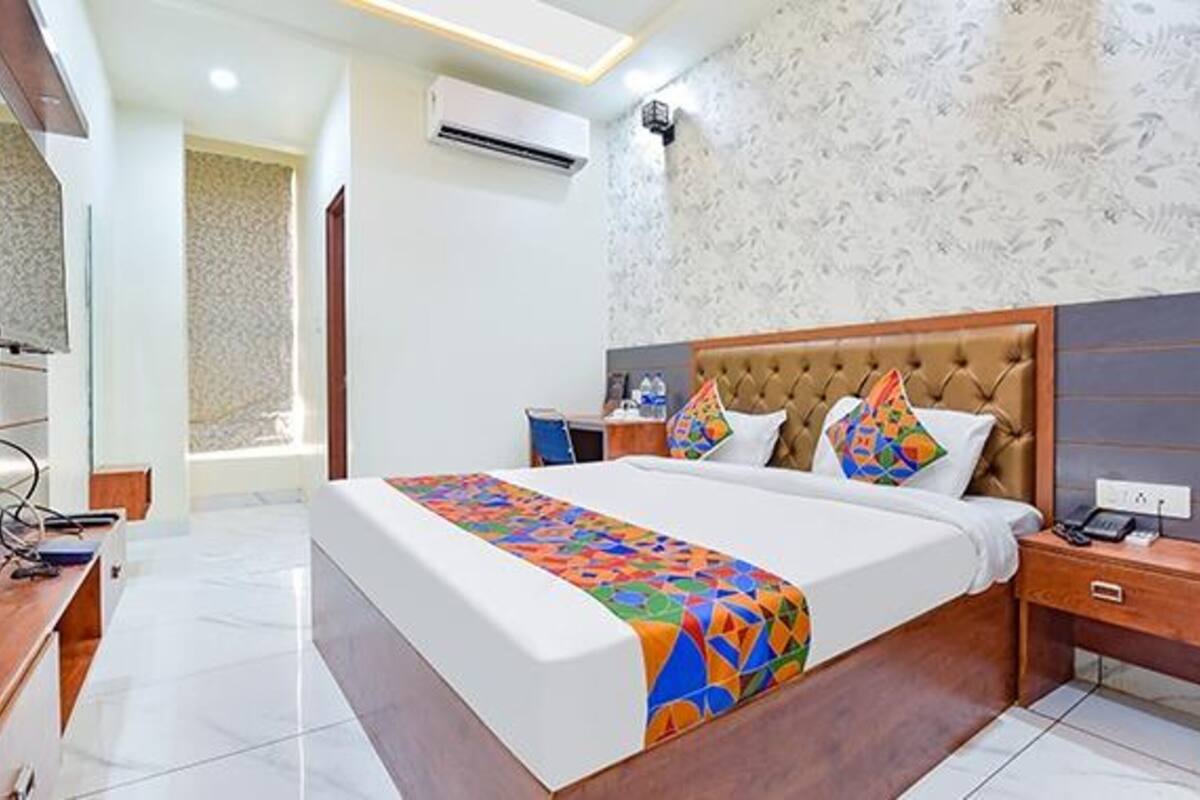 Quarto de hotel com uma cama grande, mesa de cabeceira de madeira, escrivaninha e ar condicionado fixado na parede.