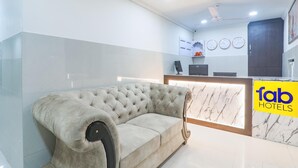Una hall d'albergo moderna con un divano trapuntato, una reception e un ventilatore a soffitto.