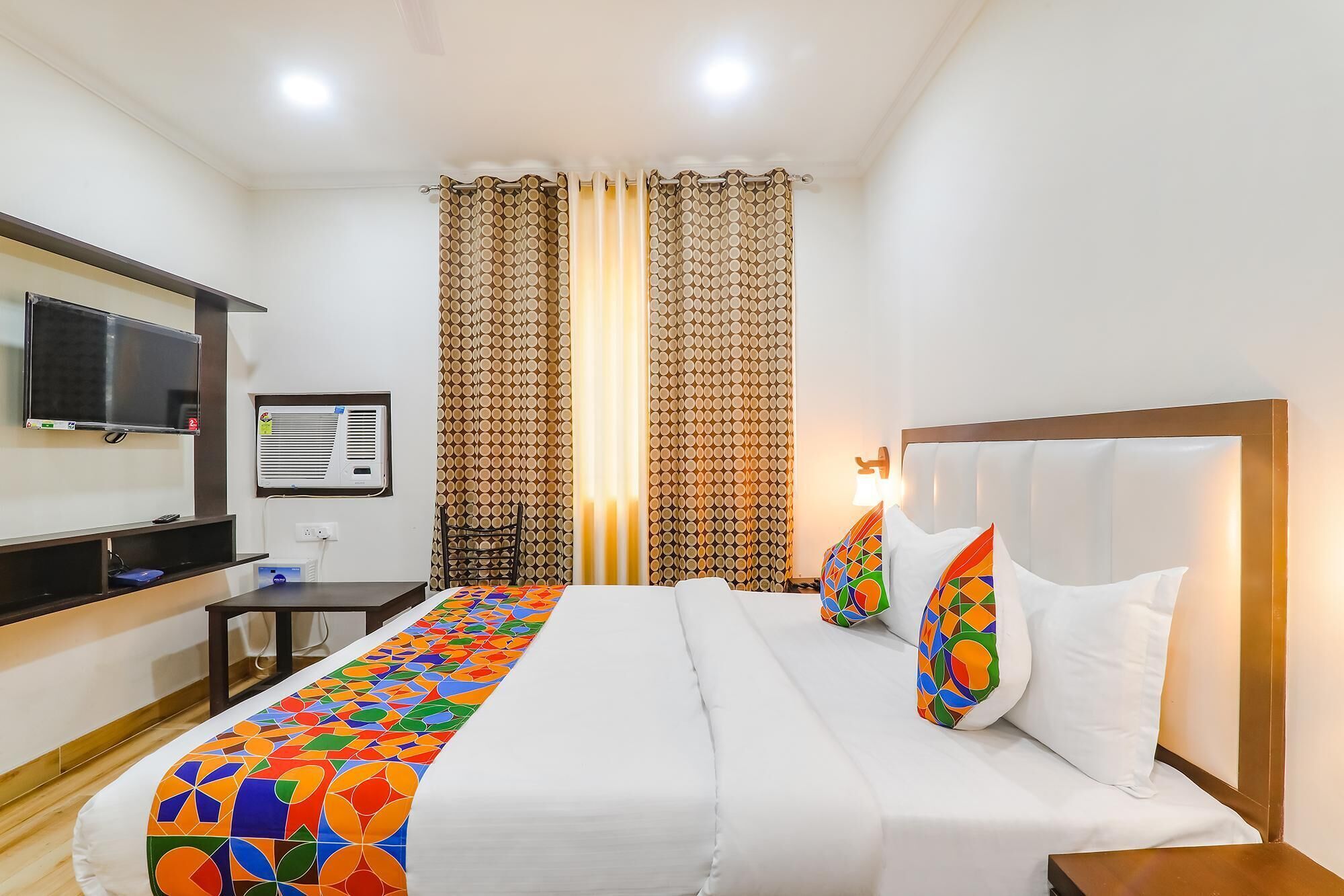 A hotel room with a bed, a TV, an air conditioning unit, and curtains.