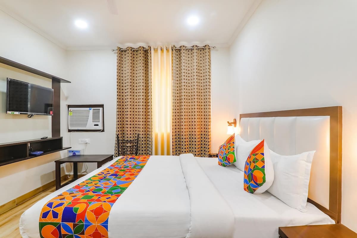 A hotel room with a bed, a TV, an air conditioning unit, and curtains.